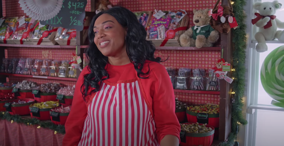 an employee at a holiday themed candy store looks on with a slightly strained smile.
